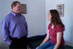 Reiki practitioner listens to client. Reiki client sits on massage table.