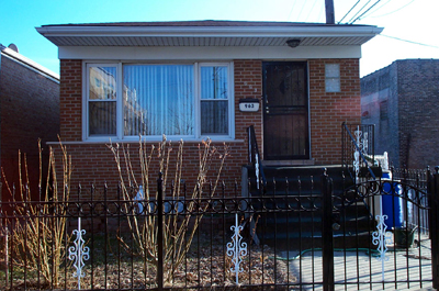 Red brick bungalow with large picture-window and wrought iron fence.